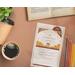 The notecard on a desk with a cup of coffee, an open book, colored pencils, and a succulent. 